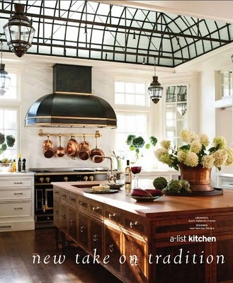 big open kitchen with black hood and stove and copper pans and pots hanging from a rack