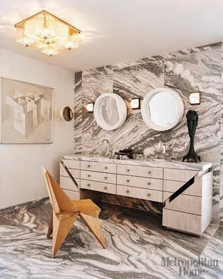 Veined Marble Bathrooms witn grey marble with heavily veins on floor and fron wall, rounded mirrors, two sinks and a dresser for vanity